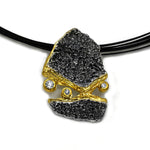 FELS Anhänger aus oxidiertem 925er Silber mit Goldakzenten an einem mehrreihigen schwarzen Band.